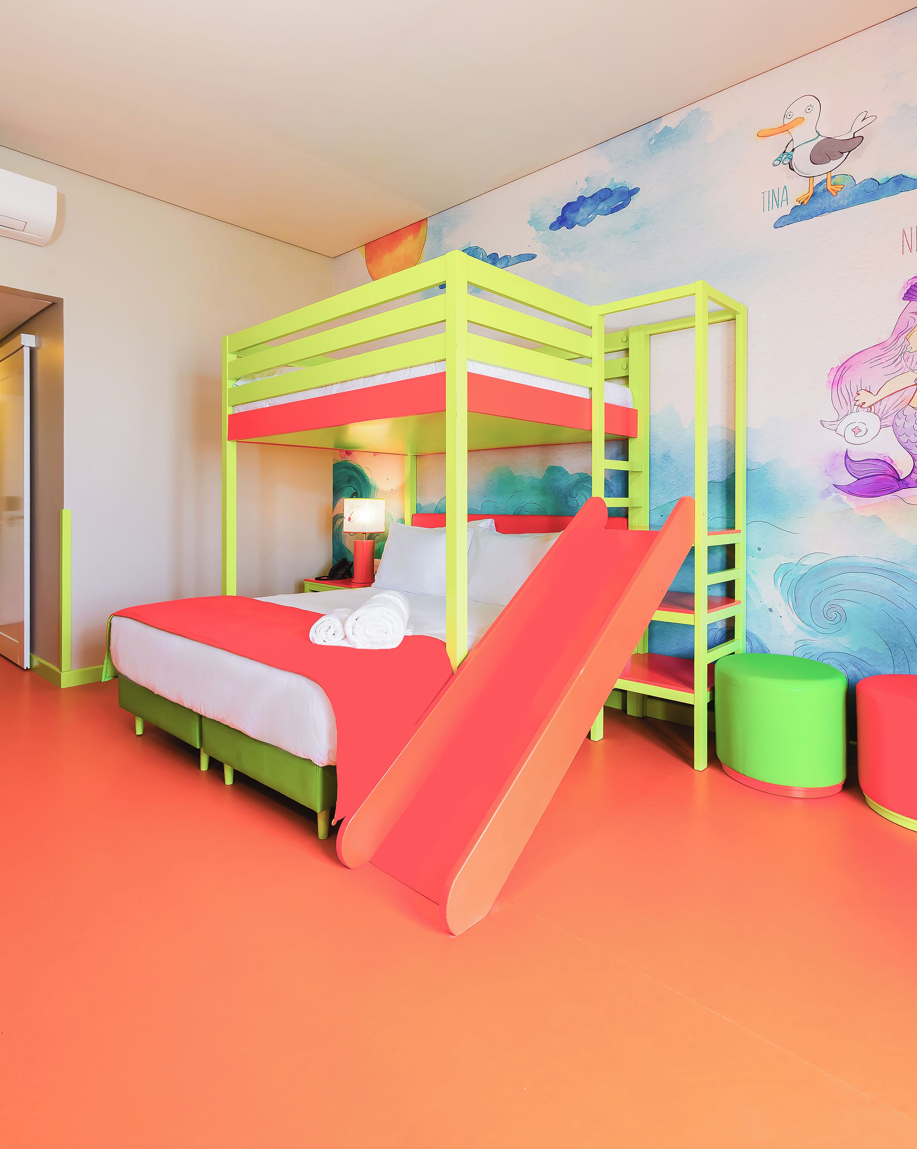 A bunk bed with a slide, a wall mural, and a green trash bin.