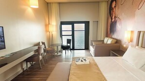 Ein Hotelzimmer mit Bett, Schreibtisch, Sessel, einer Couch und Meerblick durch ein großes Fenster.