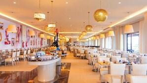 Ein großzügiger Hotel-Speisesaal mit mehreren Tischen und Stühlen, einem zentralen Buffet und großen Fenstern, die für natürliches Licht sorgen.