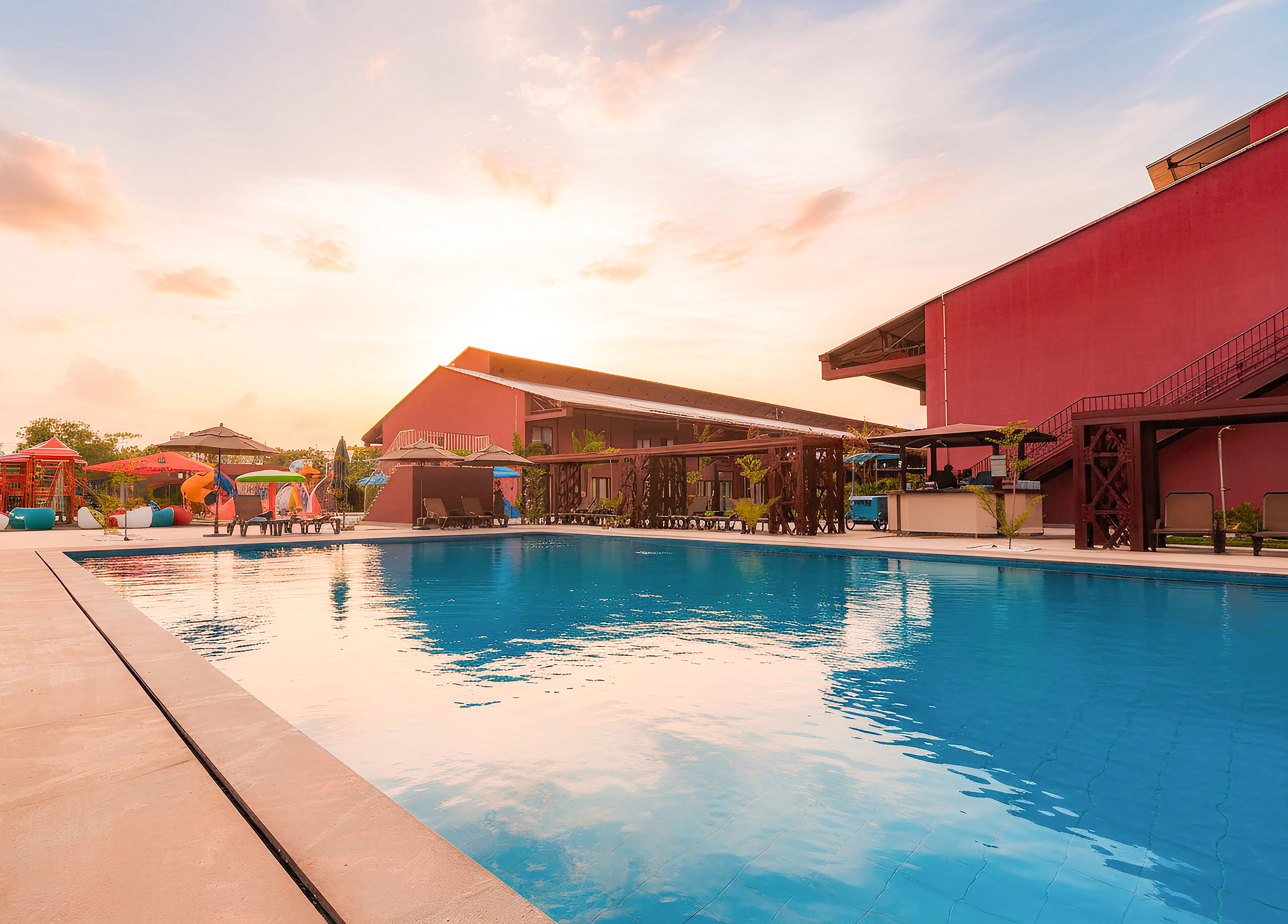 A swimming pool with lounge chairs and umbrellas, surrounded by buildings with red and beige exteriors.
