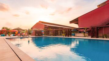 Una piscina con sillas de descanso y sombrillas, rodeada de edificios con fachadas rojas y beige.