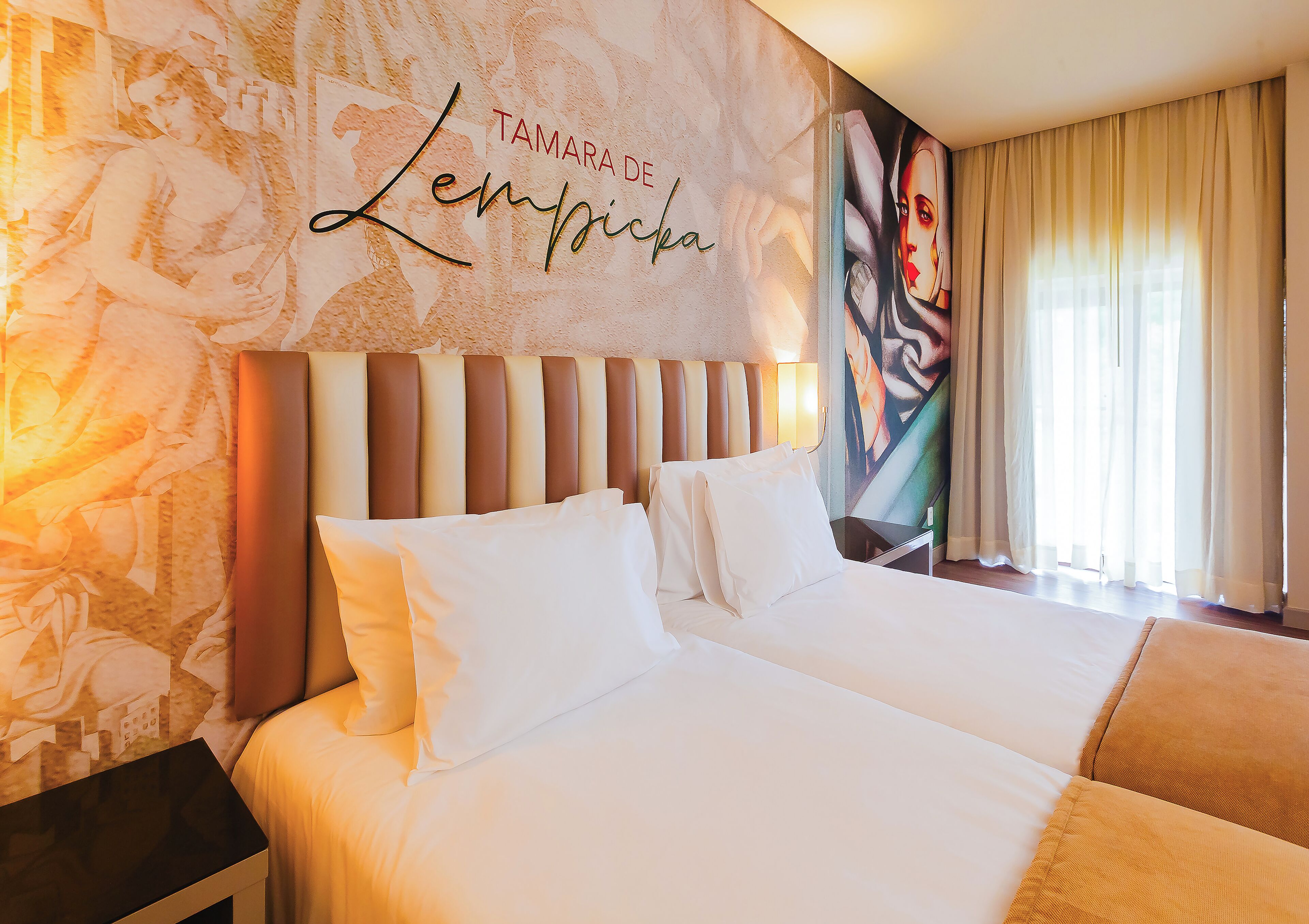 Quarto de hotel com uma cama grande, cabeceira com ripas verticais e parede com padrão floral e uma placa com nome.