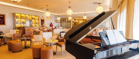Un piano de cola en un salón bien iluminado con asientos y un bar al fondo.