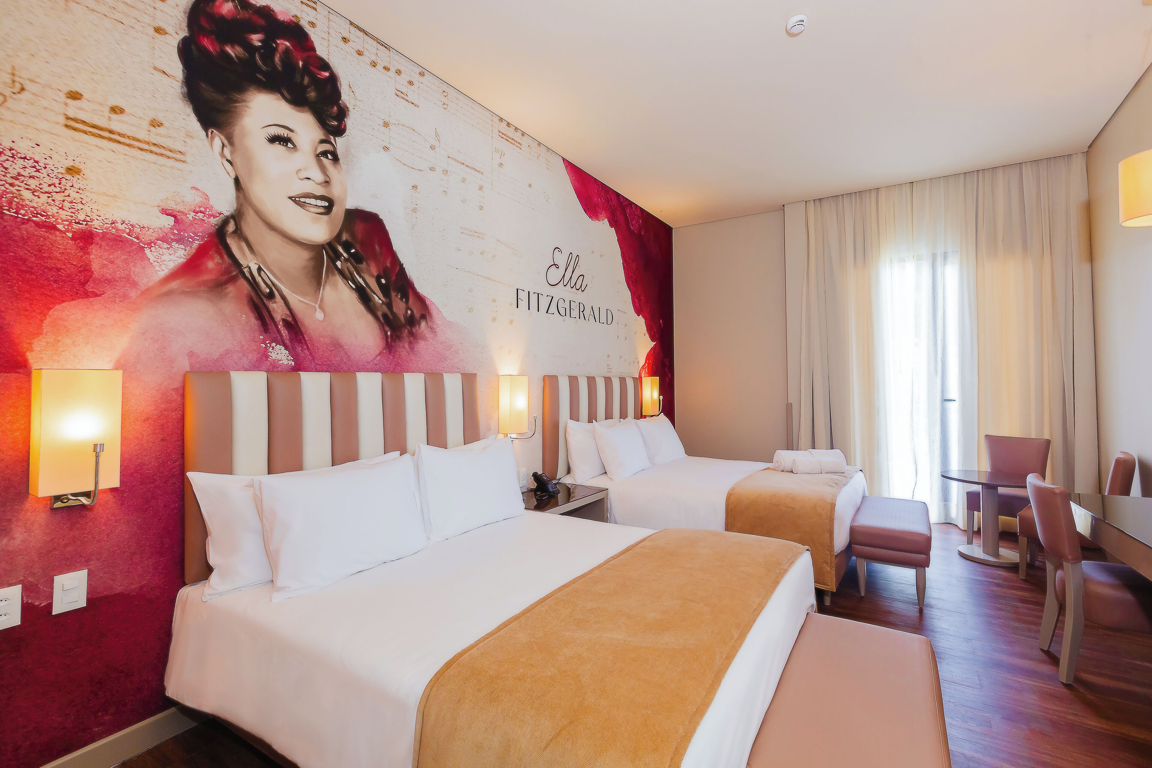 Una habitación de hotel con dos camas, un retrato grande en la pared y un rincón de comedor con mesa y sillas.