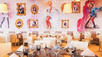 Comedor con mesas redondas dispuestas para una comida, con sillas blancas y una lámpara moderna.