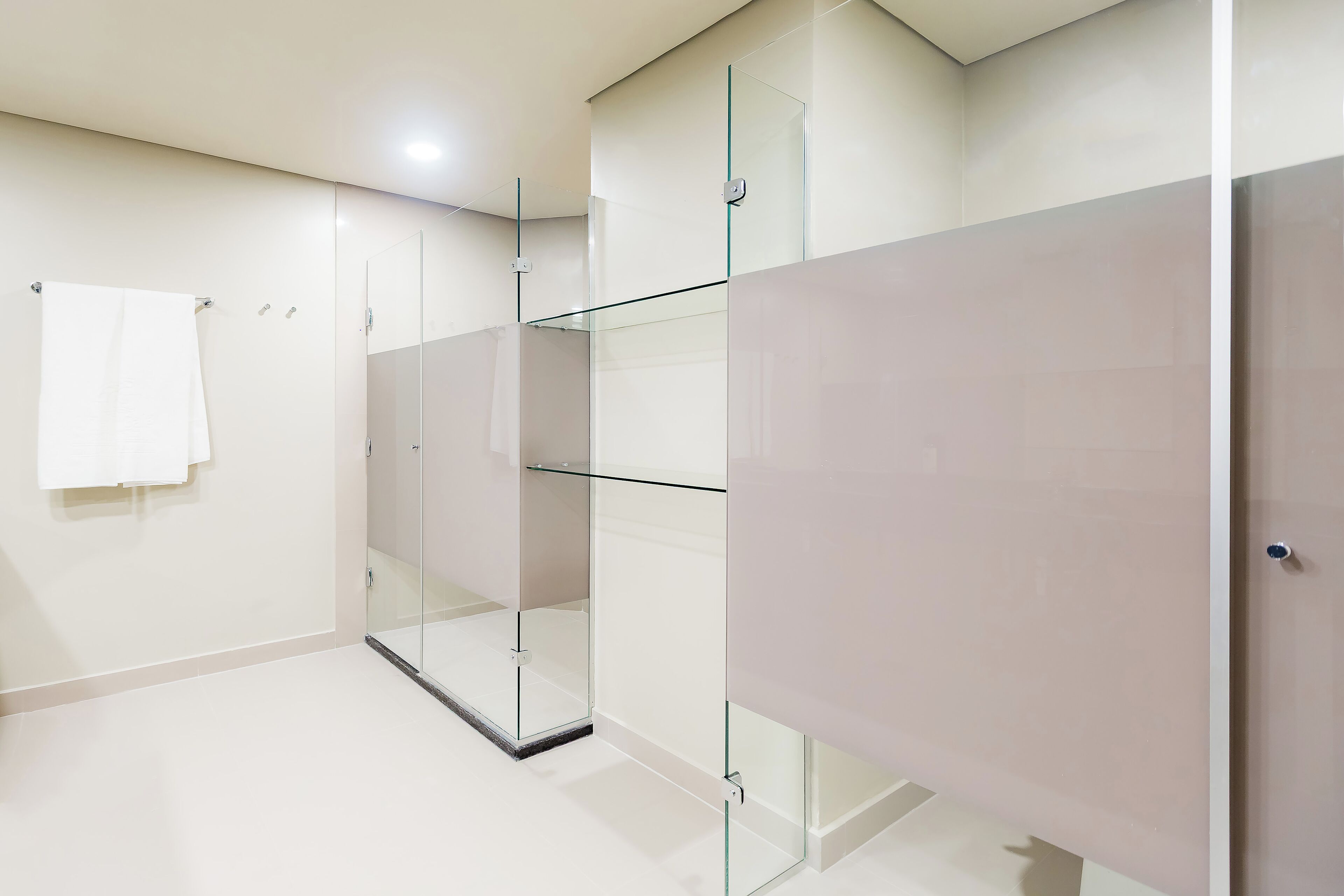 A modern bathroom with a glass shower enclosure, a white towel hanging on the wall, and a plain tiled floor.