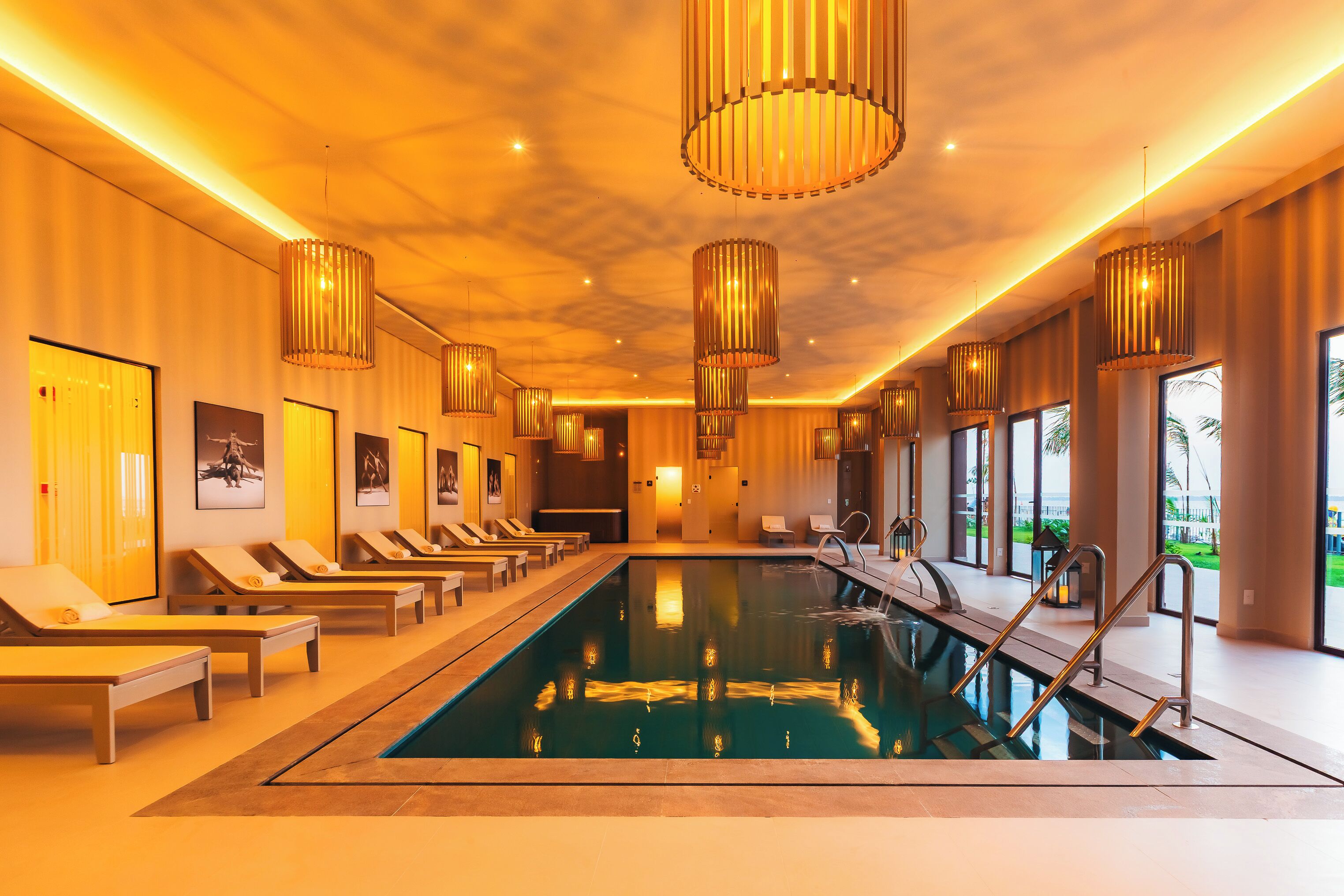 A swimming pool with lounge chairs, pendant lighting, and large windows.