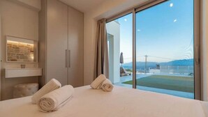 Une chambre d’hôtel moderne avec un grand lit, deux serviettes enroulées, une vue sur la mer et un balcon avec une porte vitrée.