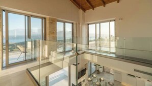 Un intérieur moderne avec de grandes fenêtres, une balustrade en verre et une vue sur l’extérieur.