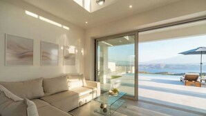 Un salon moderne avec une table basse en verre, un canapé beige et une grande porte-fenêtre coulissante donnant sur un balcon avec vue sur la mer.