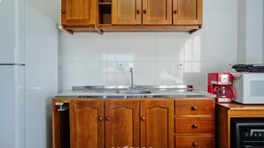 Una cocina con armarios de madera, un lavamanos de acero inoxidable, un refrigerador blanco, un microondas y una cafetera.