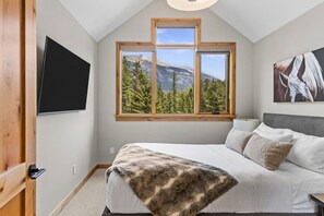 Un dormitorio con cama, televisor, ventana y vista a la montaña, además de un cuadro en la pared.
