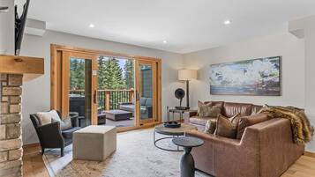 Un salon moderne avec une cheminée, un canapé, une table basse et une vue sur l’extérieur grâce à des portes vitrées.