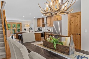 Una cucina moderna con mobili in legno, un frigorifero in acciaio inox e un originale lampadario a corna di cervo.