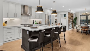 A modern kitchen with white cabinets, a central island with bar stools, stainless steel appliances, and pendant lighting. - Luxury Escape | Private Hot Tub and Firepit (Canmore)