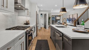 A modern kitchen with white cabinetry, stainless steel appliances, and pendant lighting. - Luxury Escape | Private Hot Tub and Firepit (Canmore)
