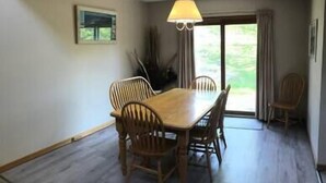 Un comedor con una mesa y sillas de madera, una lámpara colgante y vistas a zonas verdes al exterior.