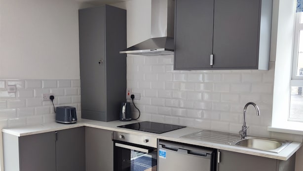 Cocina moderna con gabinetes grises, horno empotrado, lavavajillas y pileta de acero inoxidable.