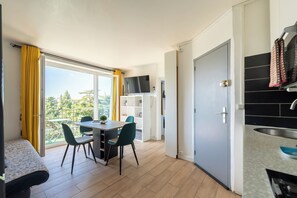 A compact living space with a balcony, a dining area, a kitchenette, and a TV mounted on the wall.