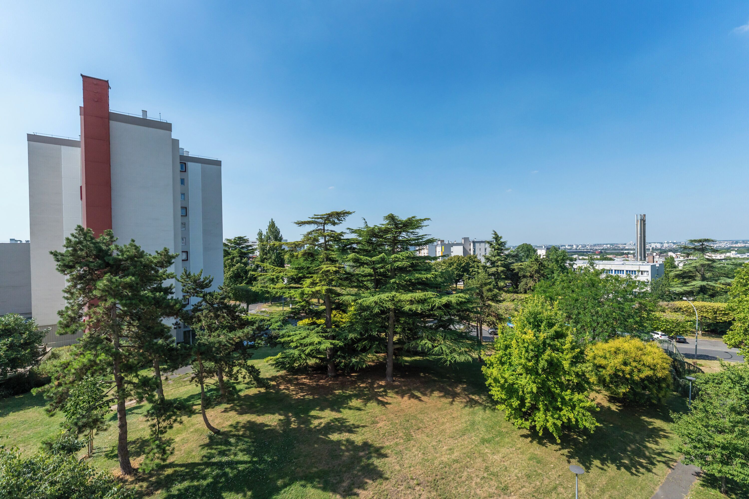 Un edificio moderno con una sezione verticale rossa, circondato da alberi e vegetazione.