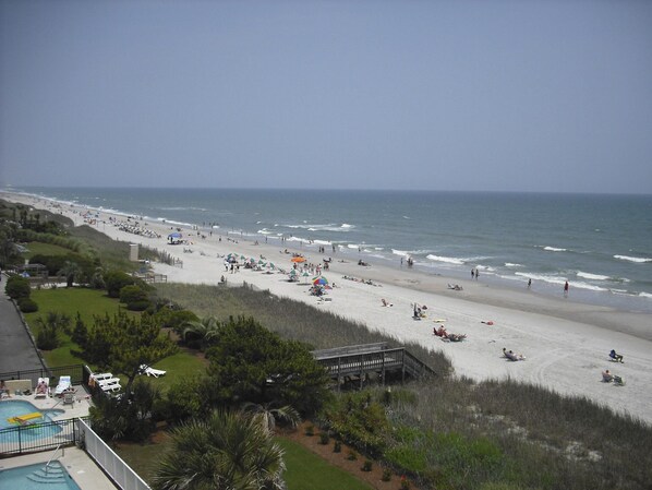 A beach with a pool area, umbrellas, and a wooden walkway.