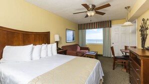 A hotel room with a large bed, a desk, a chair, a ceiling fan, and a window with curtains.