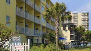 A multi-story hotel with balconies, a garden area with palm trees, and outdoor seating.