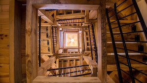 Un escalier en colimaçon en bois, doté de rampes en métal, mène à un espace central ouvert.