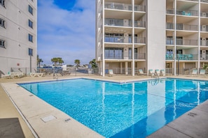 Piscina com espreguiçadeiras e um edifício com várias andares e sacadas.