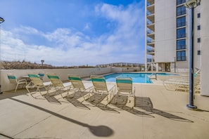 Area piscina su tetto con poltrone relax, piscina e un edificio con balconi.