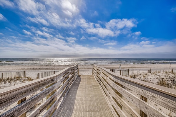 A wooden boardwalk leading to a beach with a clear sky.
