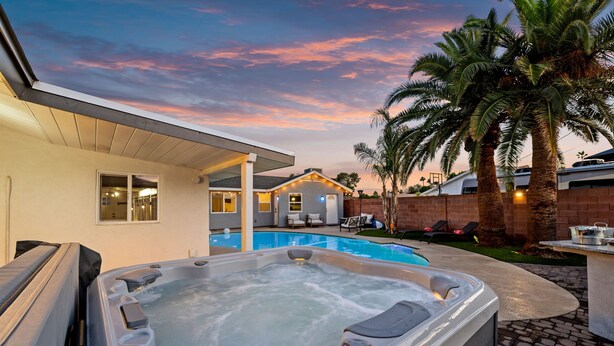 A hot tub in a backyard with a pool, palm trees, and a house with a covered patio. - Desert Oasis Retreat Pool Spa Gameroom (Scottsdale)