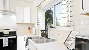 Una cucina moderna con mobili bianchi, elettrodomestici in acciaio inossidabile, un lavello doppio e una finestra con tende a righe.