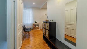 Un couloir avec un plancher en bois, un banc noir, une porte blanche et un mur blanc agrémenté d’un luminaire.