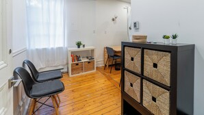 Un espace de vie compact doté d’un plancher en bois, d’un bureau avec une chaise, d’une bibliothèque et d’une petite plante posée sur une étagère.