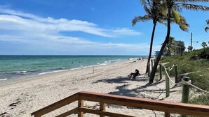 Une plage avec une promenade en bois menant au rivage, des palmiers et un ciel bleu dégagé.