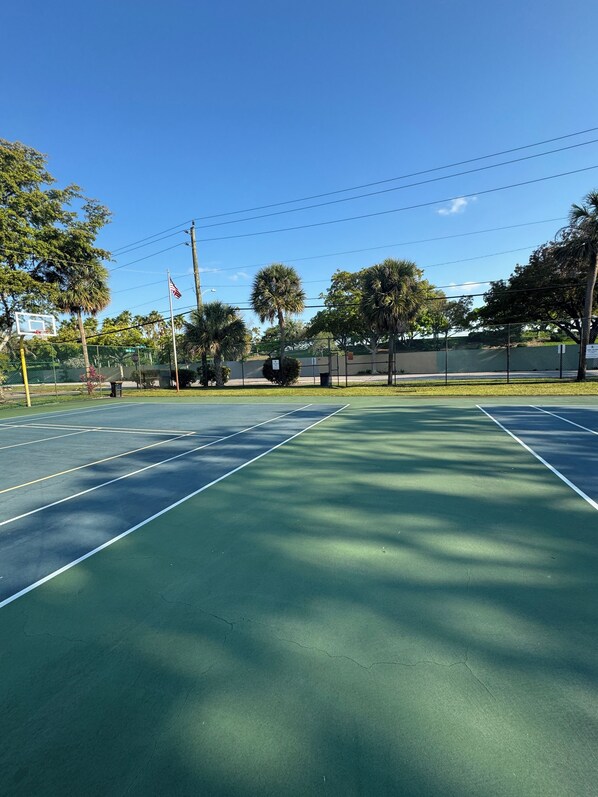 Una cancha de tenis con superficie verde, rodeada de árboles y una valla.