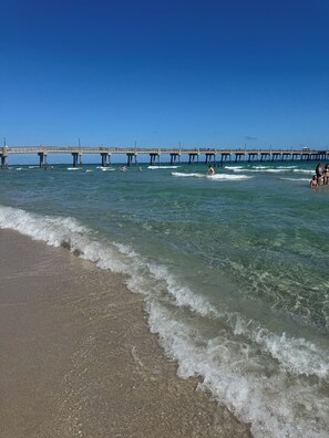 Ein Strand mit Wellen, einem Steg und Menschen im Wasser.