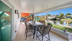 Un patio couvert avec une table et des chaises, une vue sur un plan d’eau et une terrasse en bois avec des chaises.