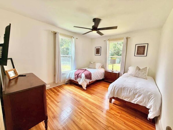 Ein Schlafzimmer mit zwei Betten, einem Deckenventilator und großen Fenstern.