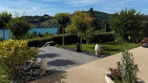 A landscaped garden with a pathway leading to a body of water, surrounded by trees and shrubs. - L'EMERAUDE suite lake view / swimming pool / beach 10 min walk away (Bilieu)