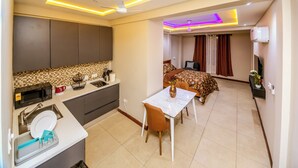 A modern hotel room with a kitchen, dining area, and a bedroom with a bed and curtains. - Davina's Villa - Beloved Retreat Studio Apt2 (Kumasi)