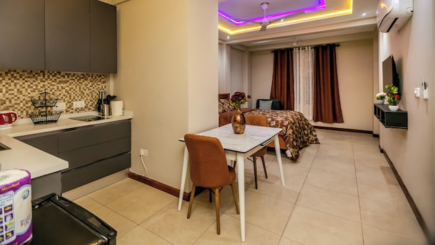 A modern kitchen with a dining area, a ceiling fan, and a TV mounted on the wall. - Davina's Villa - Beloved Retreat Studio Apt2 (Kumasi)