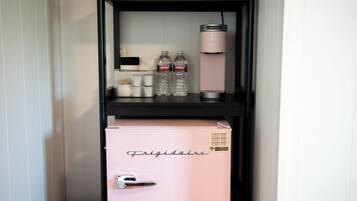 A pink minibar with a 'Frigidaire' label, two water bottles, and a pink thermos on a black shelf.