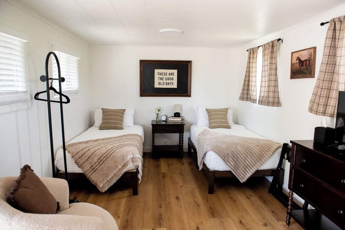 A room with two beds, a dresser, a coat rack, and a framed quote on the wall.