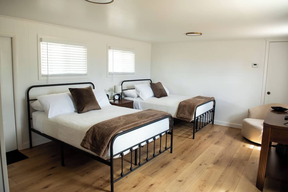 A bedroom with two beds, a wooden floor, and a small table.