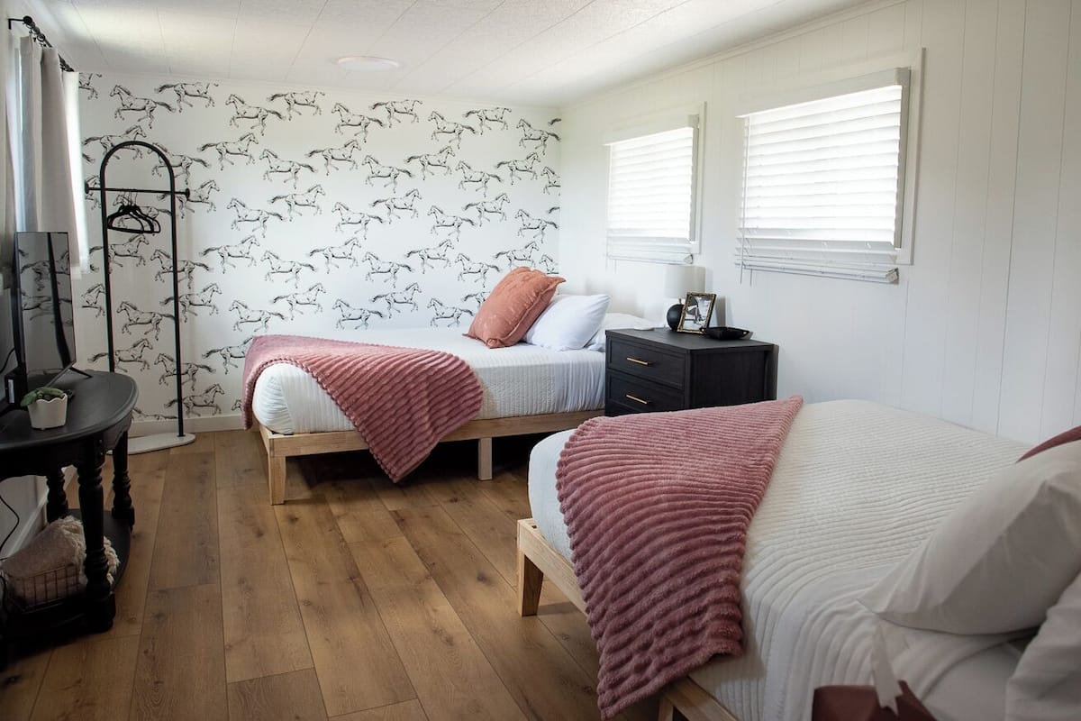 A bedroom with two beds, a wooden floor, a wall with horse patterns, and a window with blinds.