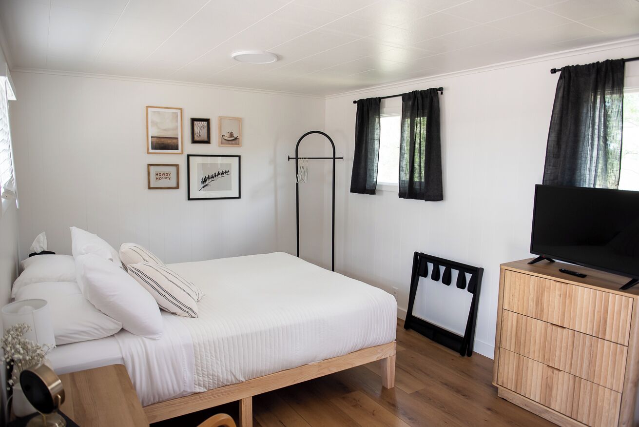 A bedroom with a bed, a TV, a wardrobe, and a window with curtains.