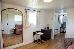 A room with a large mirror, a vanity with a stool, a pink sofa, and a black dresser. - Motel Miles (Miles City)