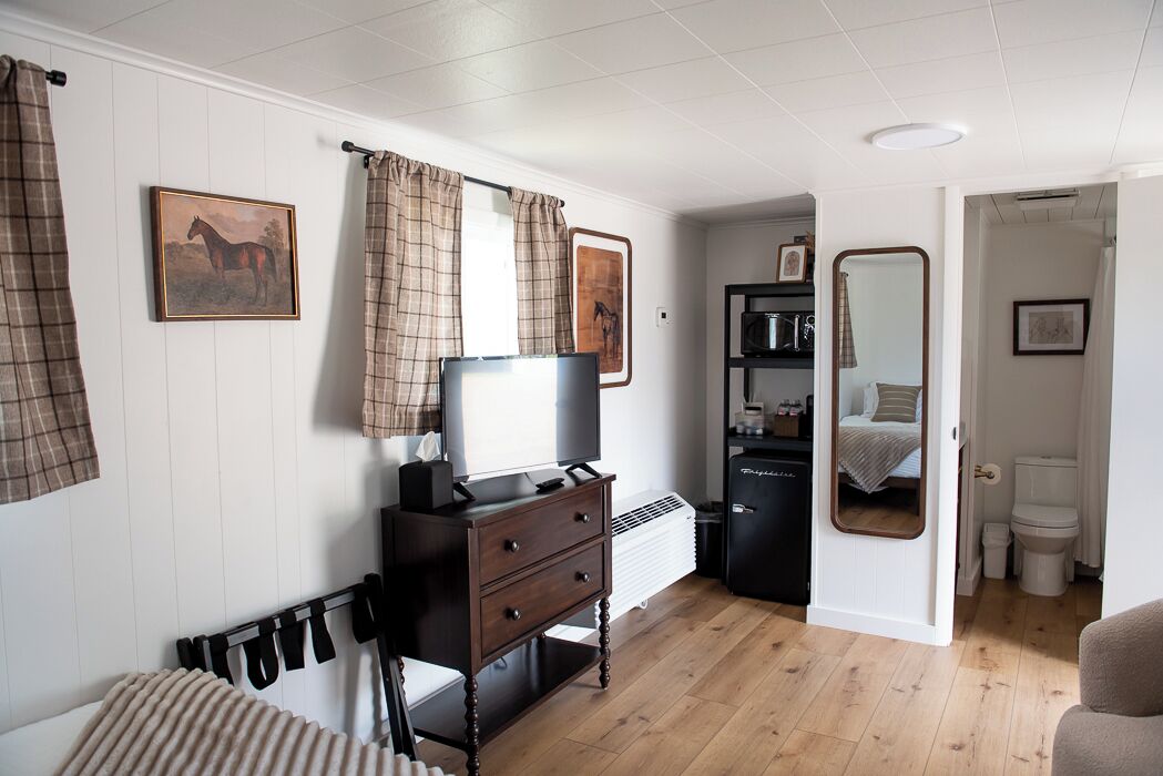A bedroom with a bed, a dresser, a TV, a mirror, and a bathroom visible through an open door.